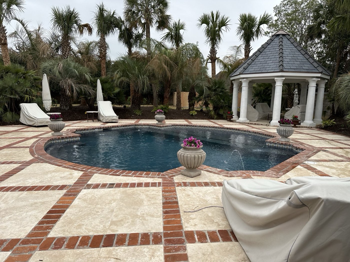Freeform pool with brick and travertine deck, gazebo, and palms
