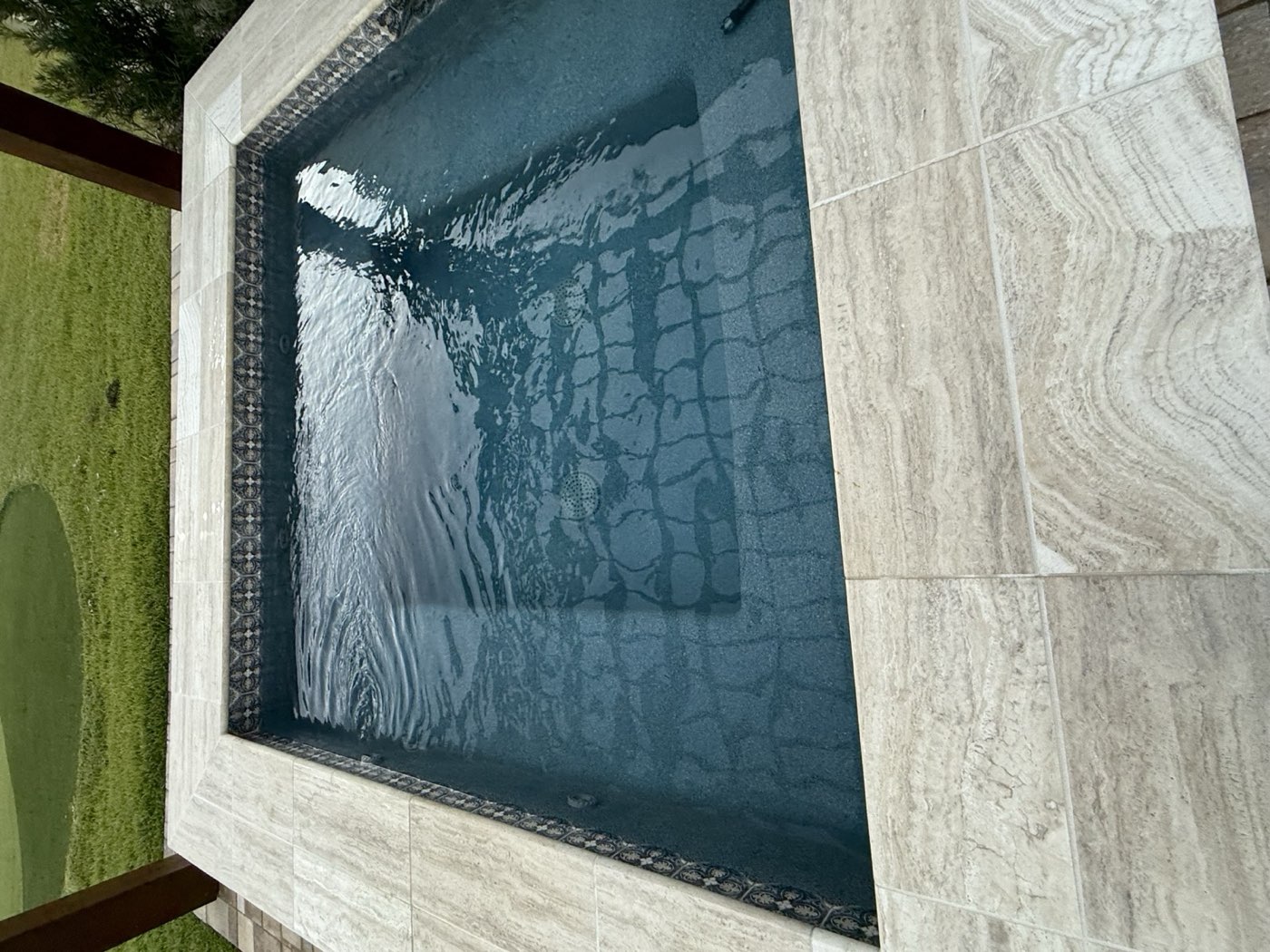 Square spa with decorative tile and travertine surround
