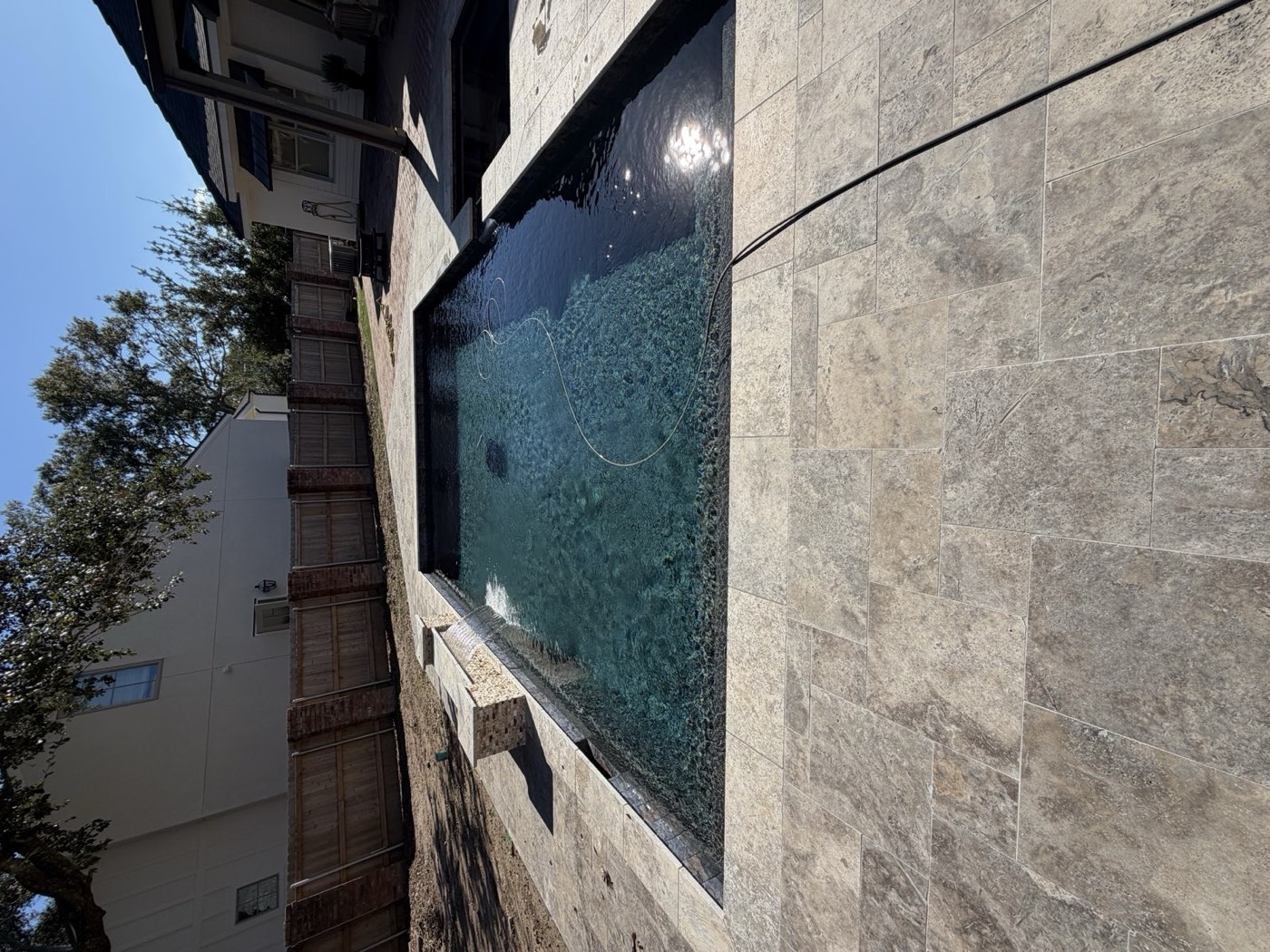Rectangular pool with sheer descent water feature and travertine deck